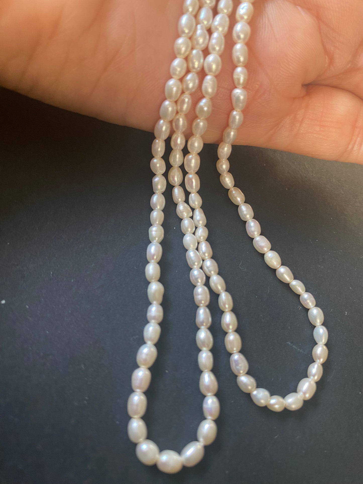 A hand delicately holds a strand of 3-3.2mm freshwater rice pearls, showcasing their lustre and elegance