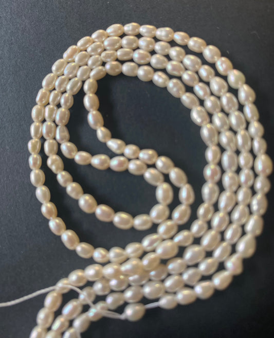 A beautiful strand of 3.0-3.2mm freshwater rice pearls resting on a sleek black background, showcasing their lustre.