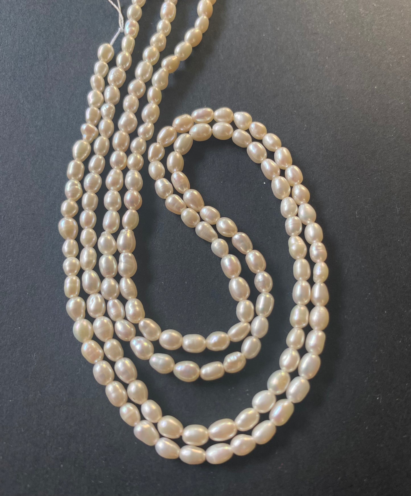 A strand of lustrous 3.0-3.2mm freshwater rice pearls laid out on a dark black surface, highlighting their elegance.