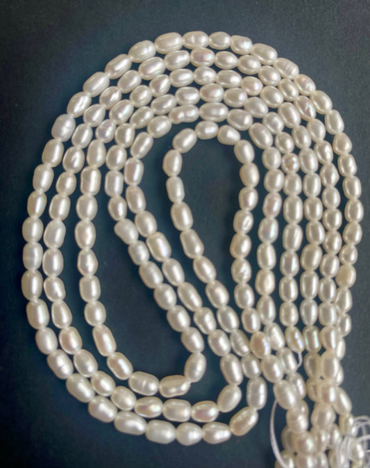 Strands of freshwater rice pearls, measuring 3.1-3.5mm, elegantly arranged on a dark surface.