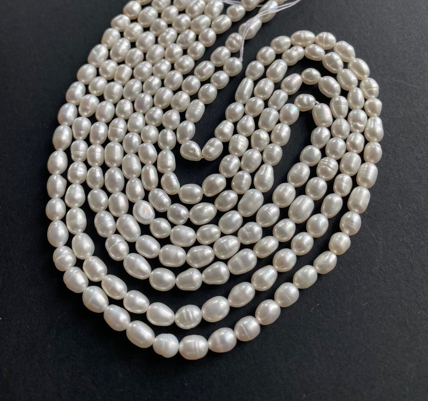 Strand of lustrous 4-4.5mm freshwater rice pearl beads laid out on a dark black surface, highlighting their elegance.