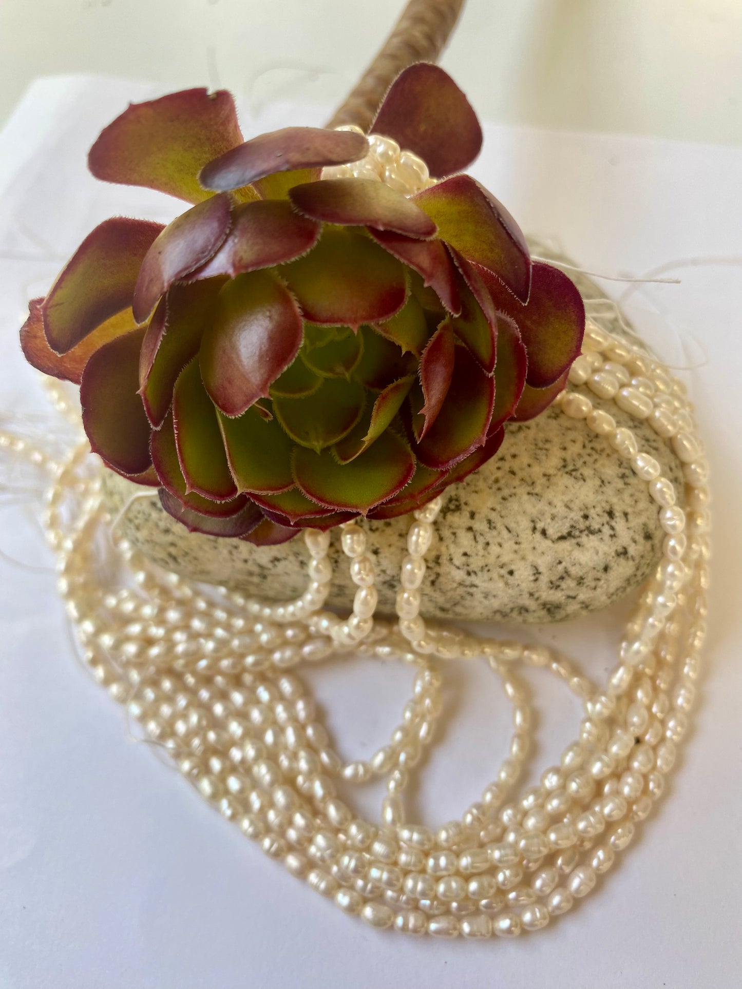 Small freshwater rice pearls, measuring 2-2.5mm, displayed on a sleek white surface.