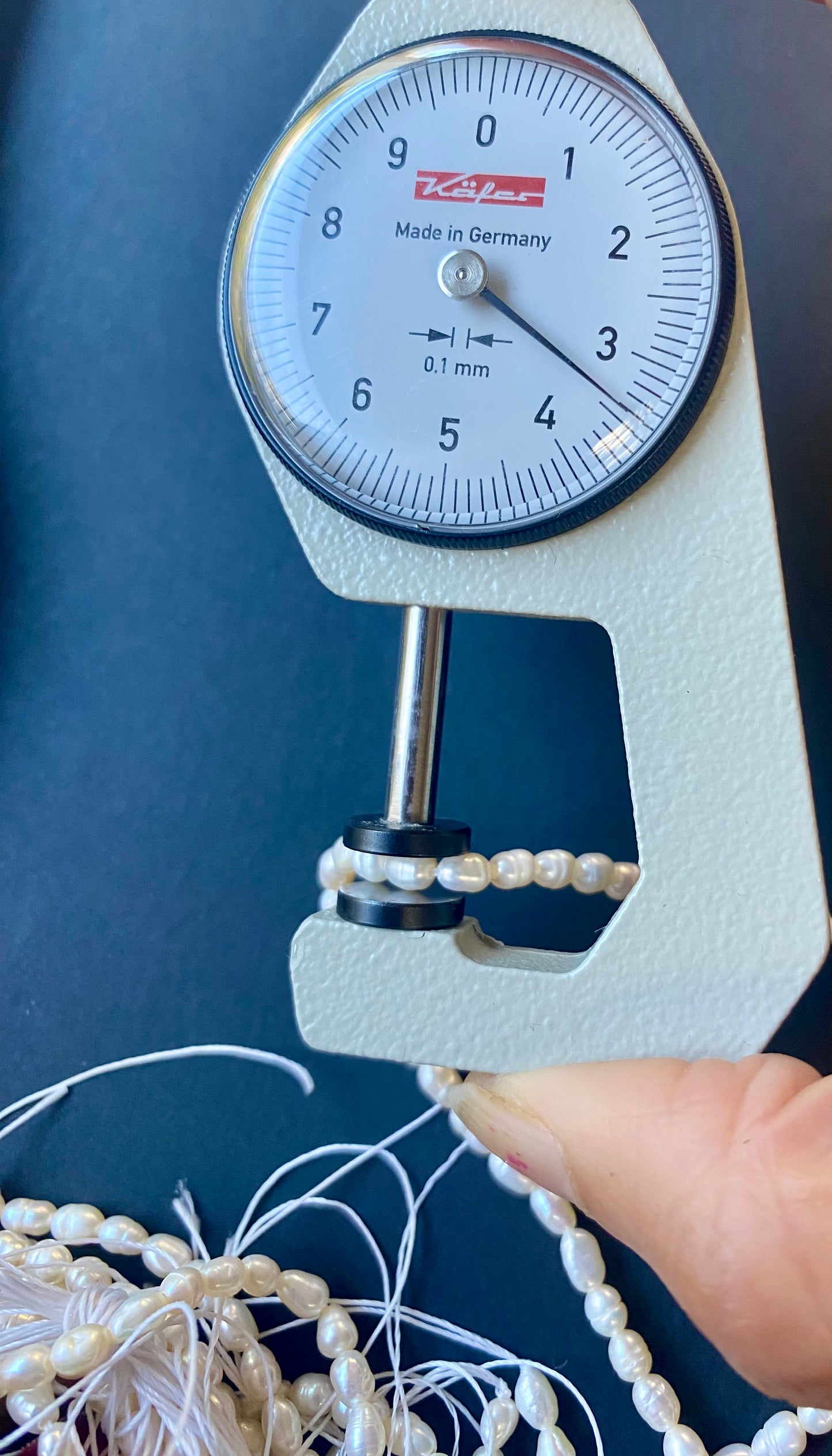 A hand holds a measuring dial gauge next to a string of 3.5mm freshwater rice pearls, highlighting their elegance and size.