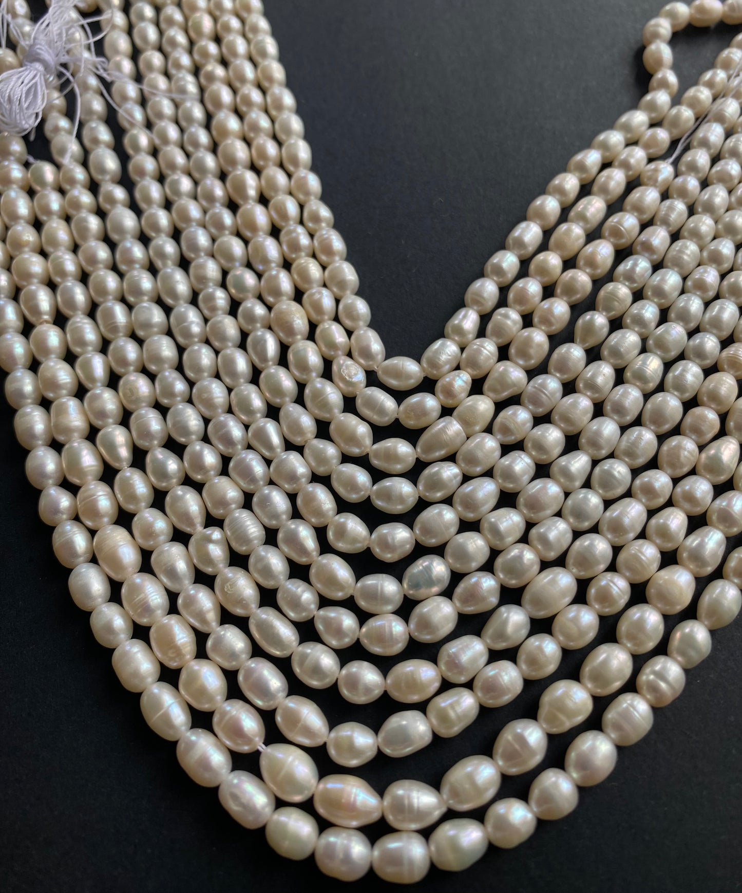 Strands of lustrous freshwater rice pearl beads laid out on a dark black surface, highlighting their elegance.