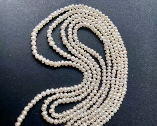 A beautiful strand of 3mm freshwater rice pearls resting on a sleek black background, showcasing their lustre.