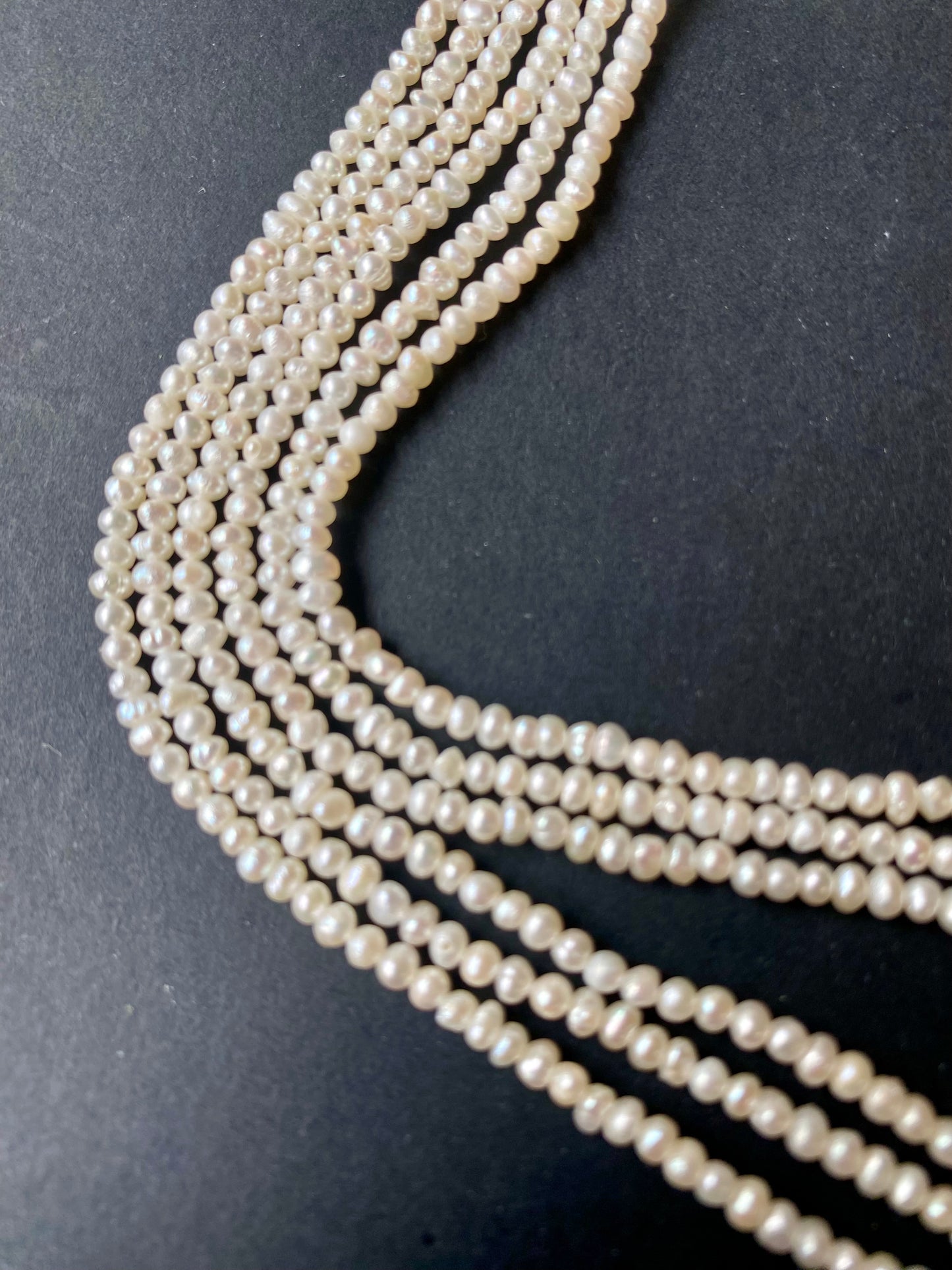 A delicate strand of 3mm freshwater rice pearls elegantly displayed on a smooth black surface.