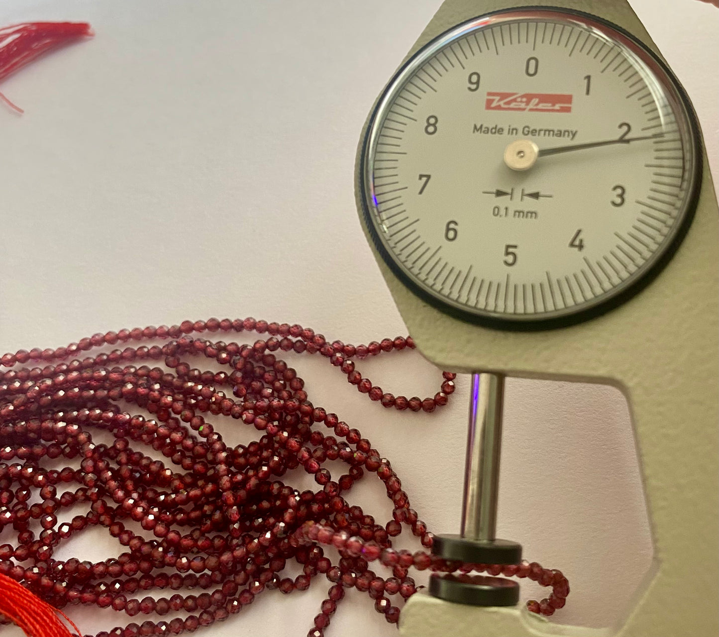 Close-up of a measuring dial gauge tool alongside a string, highlighting the precision of measurements for Garnet jewellery.