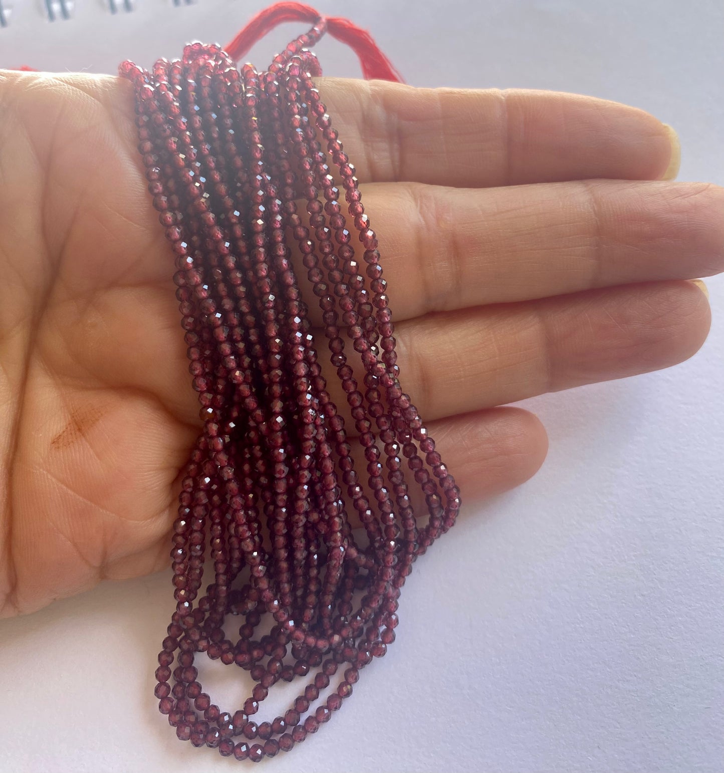 A person holding a faceted strand of Garnet rondelle beads, measuring 2.2mm, showcasing their elegant red colour.