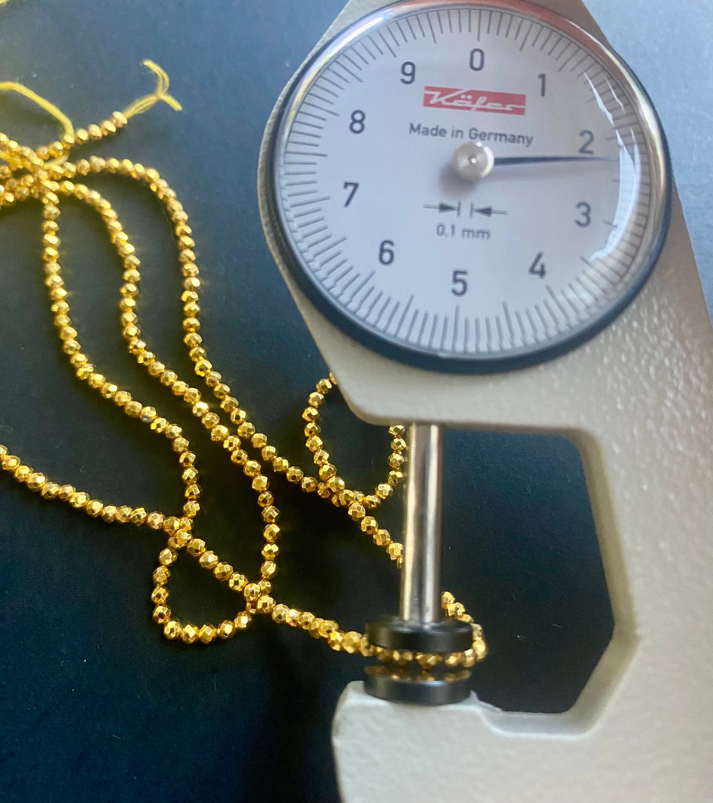A dial gauge displaying a gold pyrite bead beside a gold gemstone strand made of faceted rondelle spinel beads, 3-5mm in size.