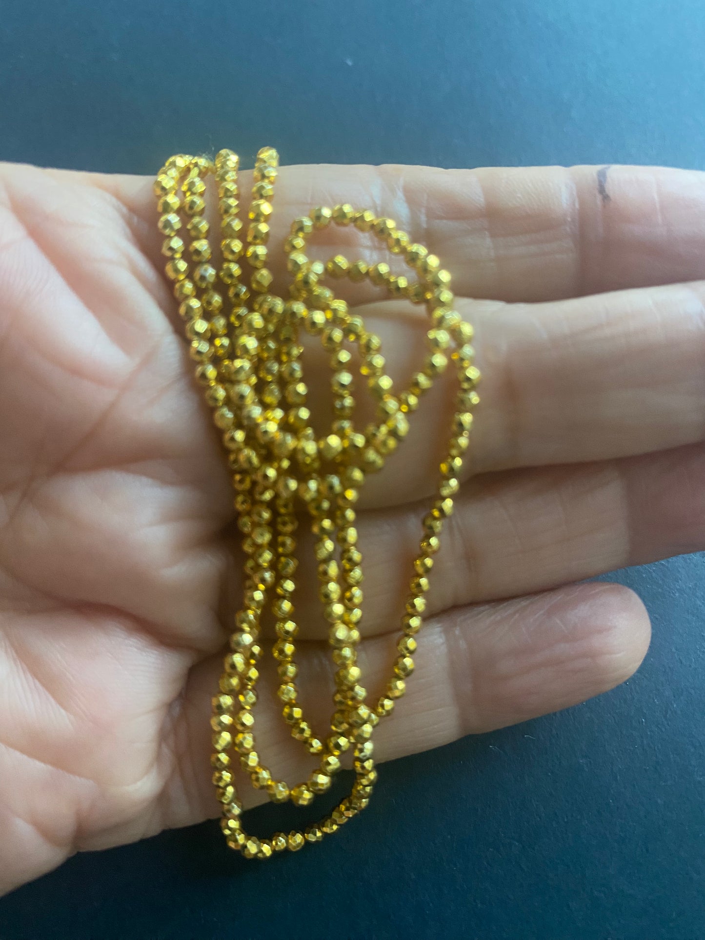 A person holding a strand of gold pyrite faceted rondelle beads, measuring 3-5mm in size.
