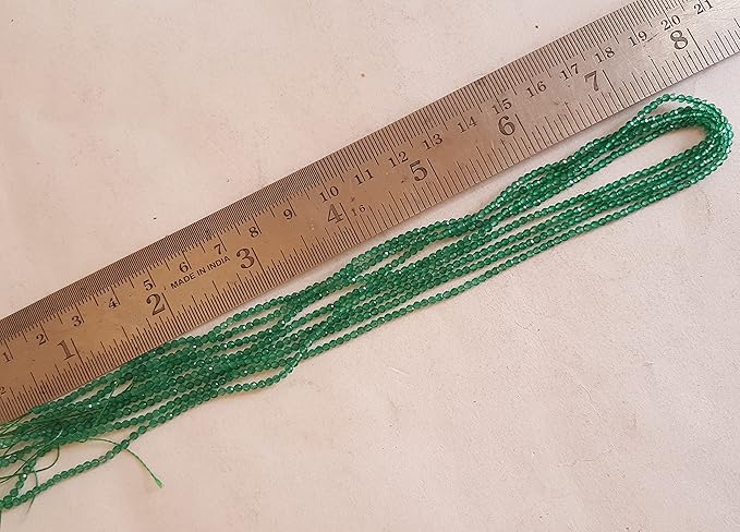 Close-up of a ruler ealongside green onyx beads, showcasing their faceted rondelle shape and size.