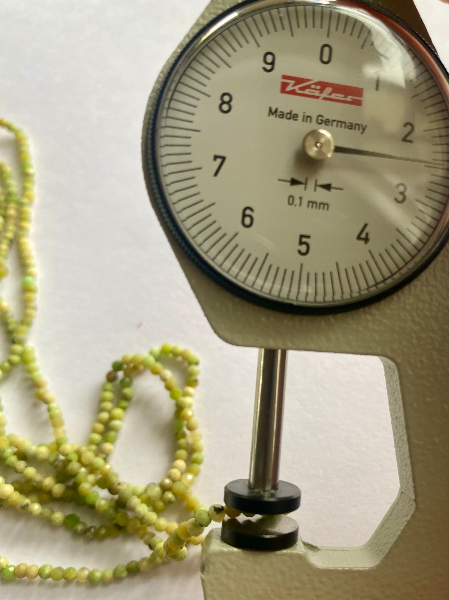 A dial gauge displaying a green bead beside a green gemstone strand made of faceted rondelle opal beads, 2.5mm in size.