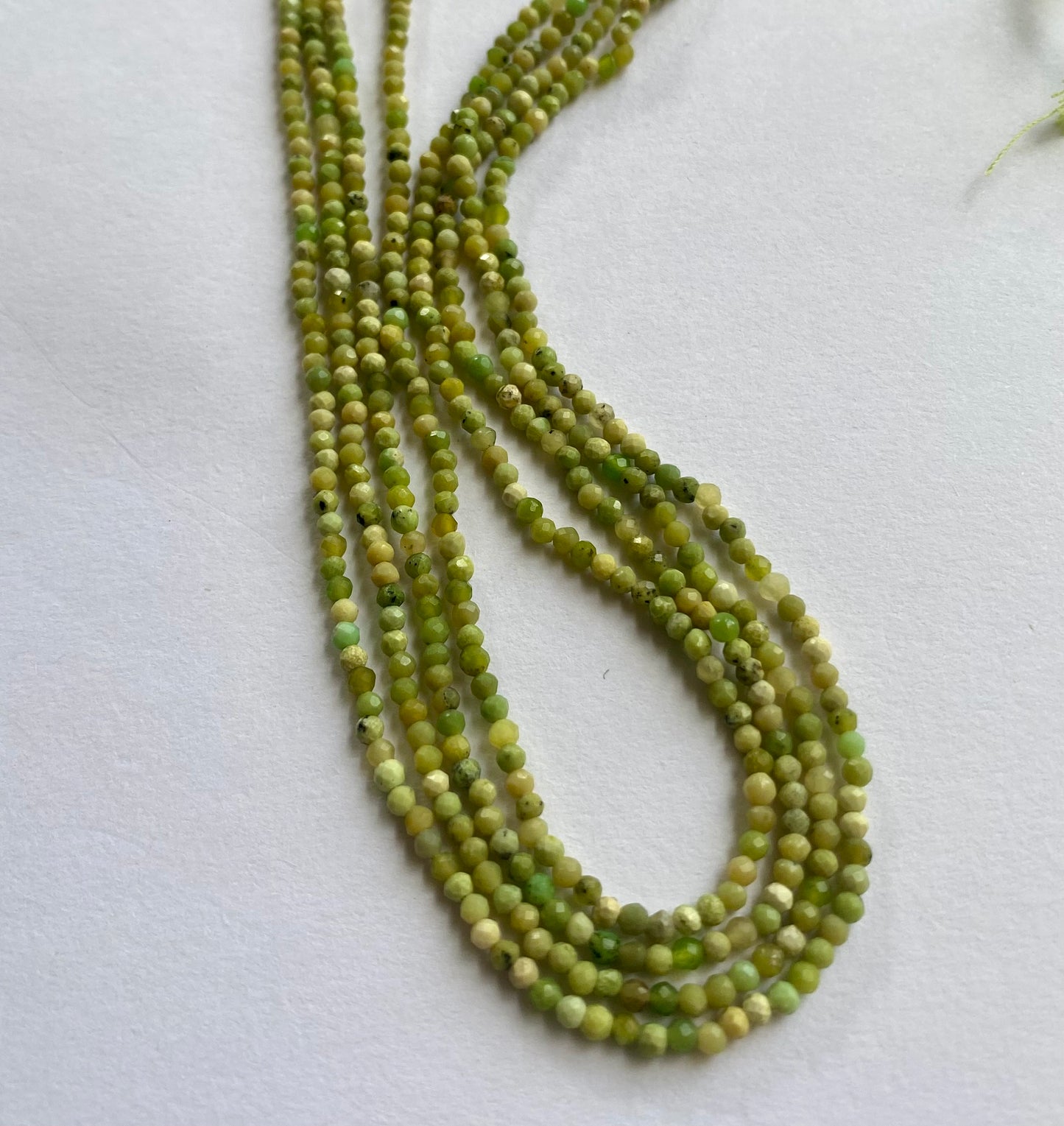 A beautiful strand of 2.5mm green opal beads resting on a sleek green background, showcasing their lustre.