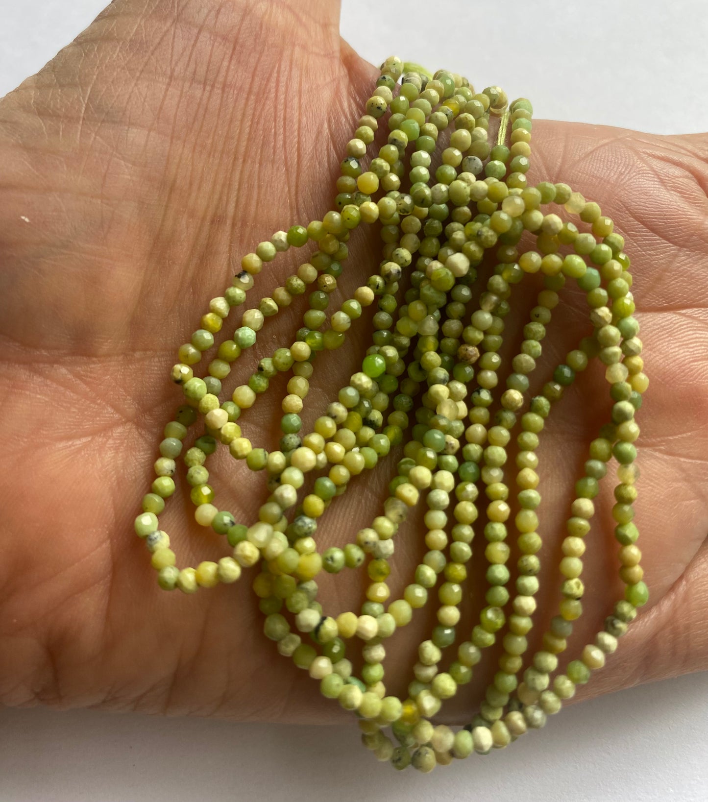 Close-up of a person’s hand holding a delicate strand of 2.5mm green opal faceted rondelle beads.