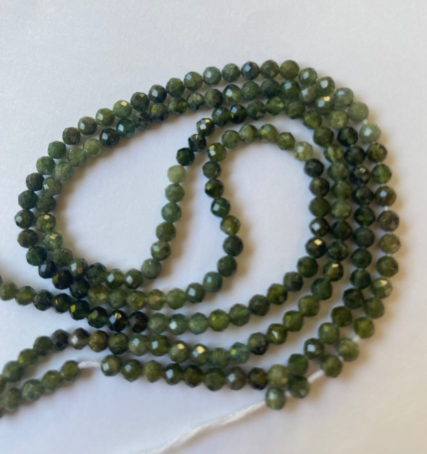 Green faceted Tourmaline beads, 3.5mm in size, arranged on a white surface, showcasing their vibrant colour and texture.