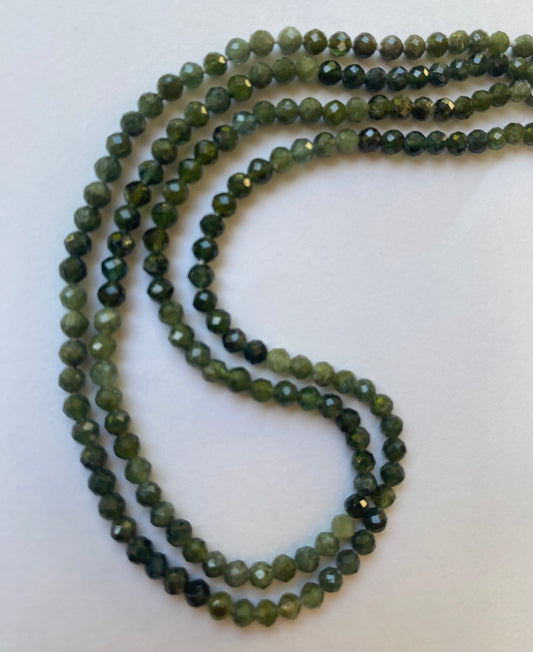 A collection of 3.5mm green faceted Tourmaline beads displayed on a white surface, highlighting their rich green hue.