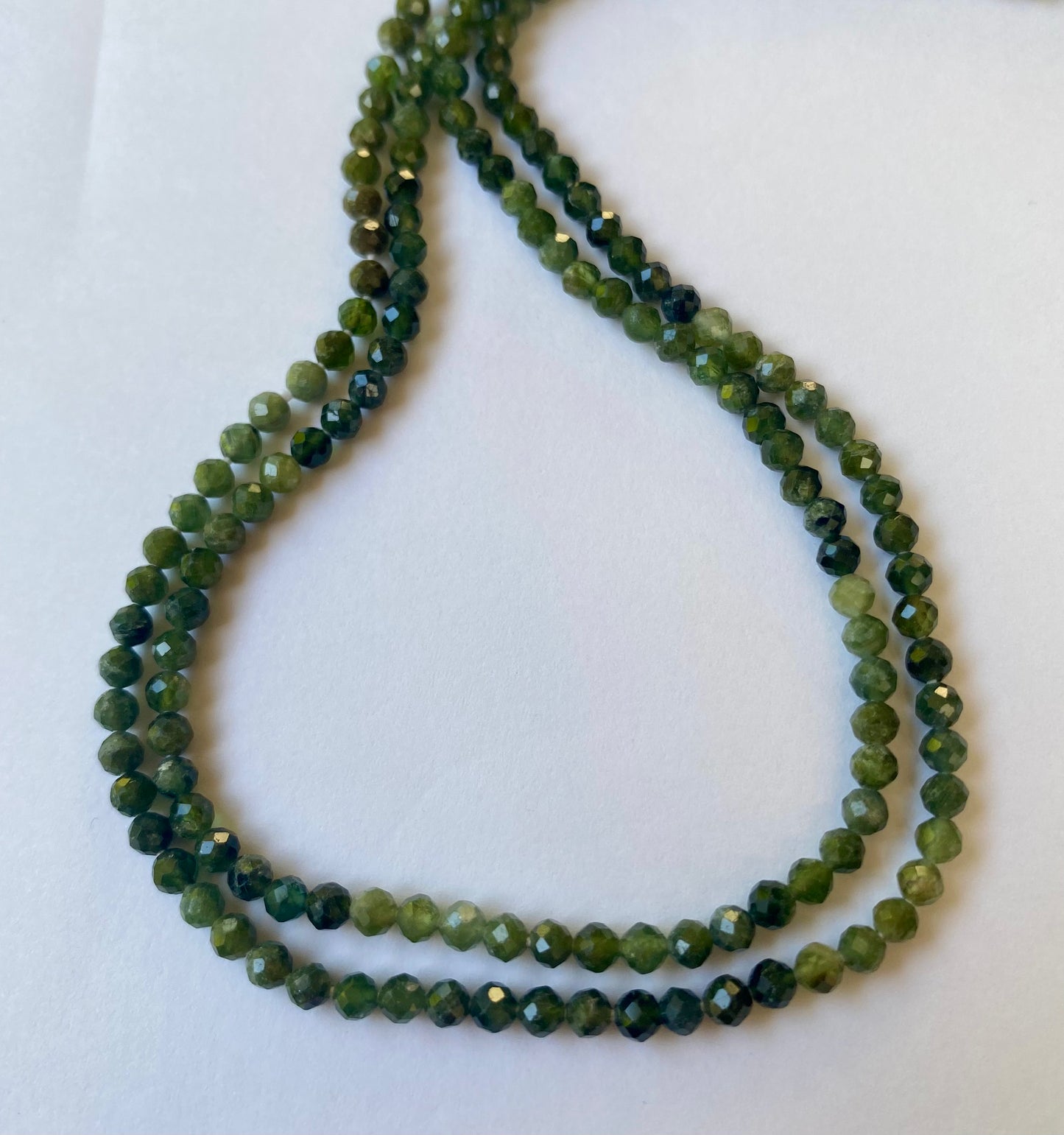 Close-up of green faceted tourmaline beads, 3.5mm, set against a white background, emphasising their colour and shine.