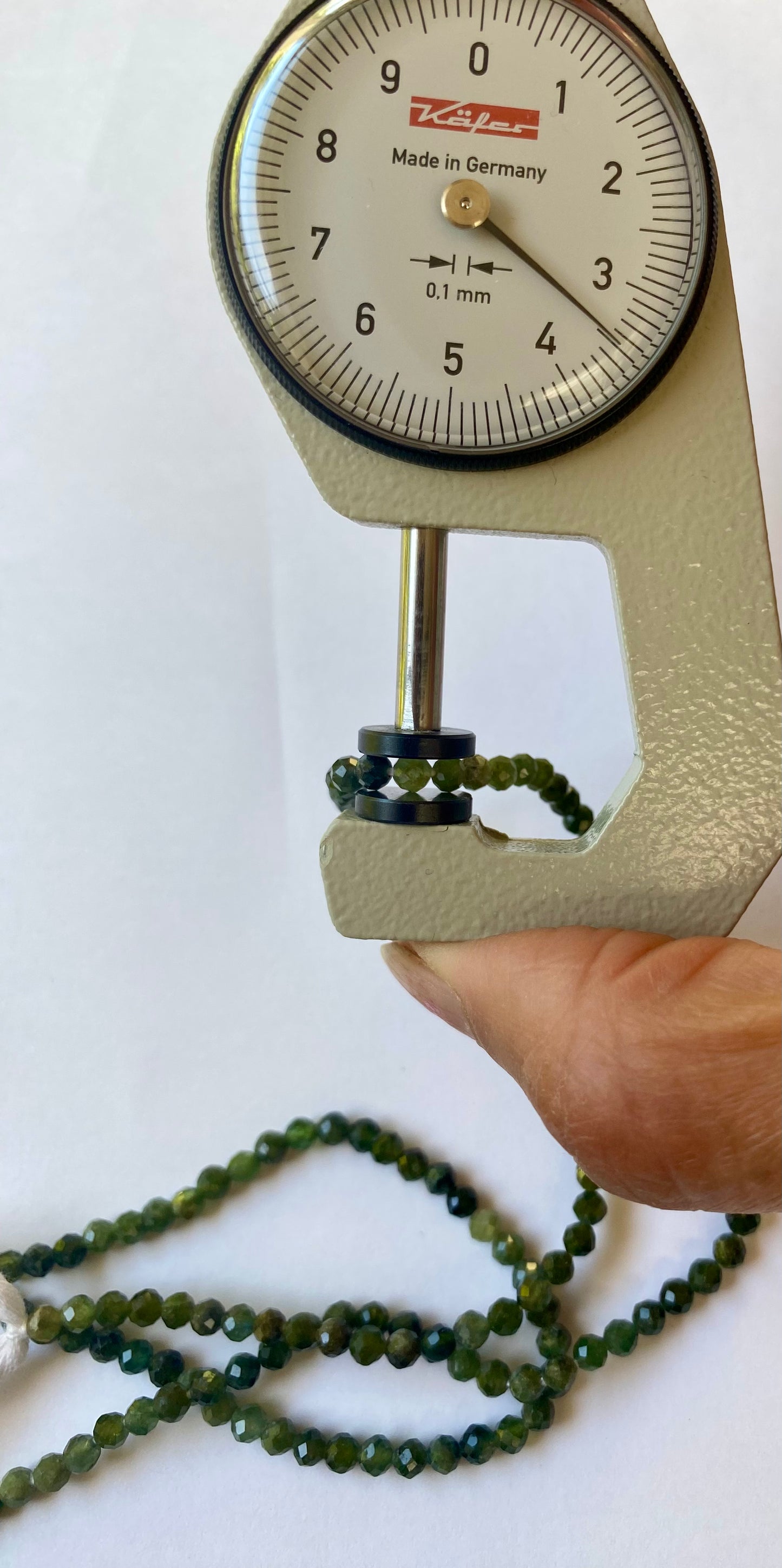 A person holds a gauge displaying a 3.5mm green tourmaline bead, showcasing its size and colour.