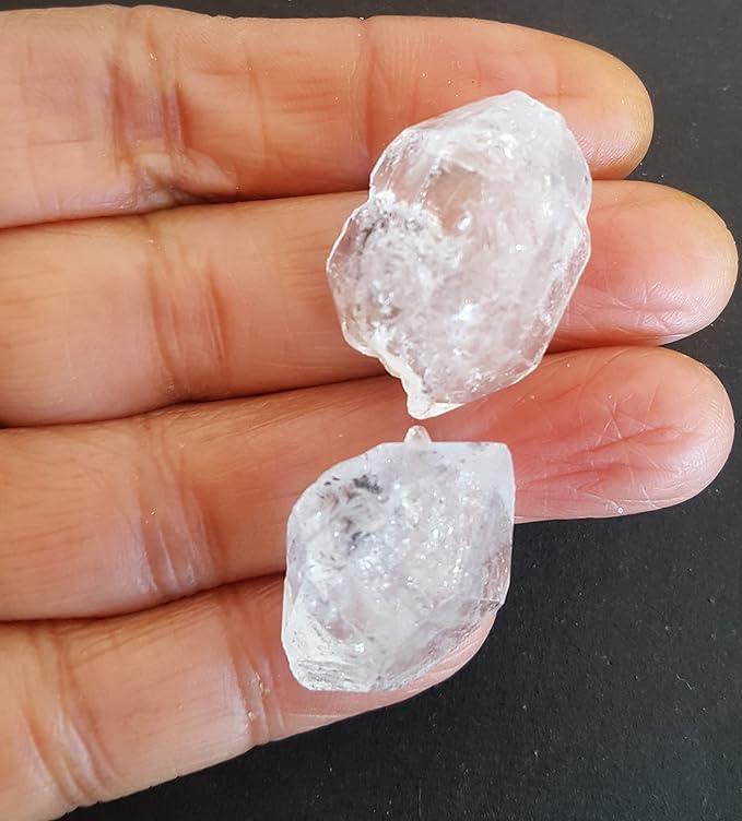 In a hand, two large Herkimer Diamond crystals shine, emphasising their clarity and the beauty of undrilled gemstones.