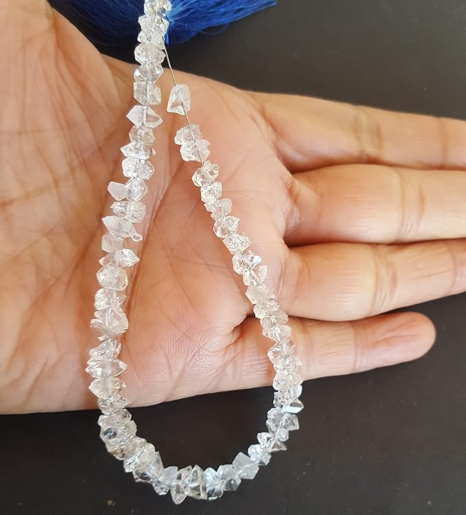 A hand holding a cluster of Herkimer Diamond gemstone beads, showcasing their rough texture and vibrant colour.