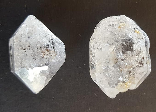 A pair of clear Herkimer Diamond, loose gemstone, displayed on a sleek black background.