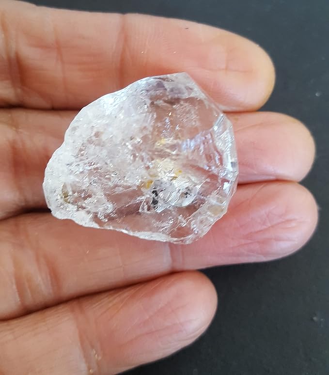 A rough Herkimer diamond gemstone bead displayed in a person's hand highlighting its unique shape and brilliant clarity.