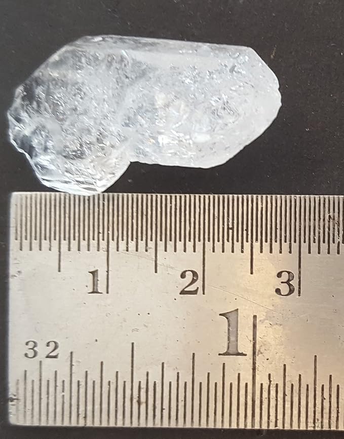 A ruler beside a rough Herkimer diamond gemstone displayed on a table.