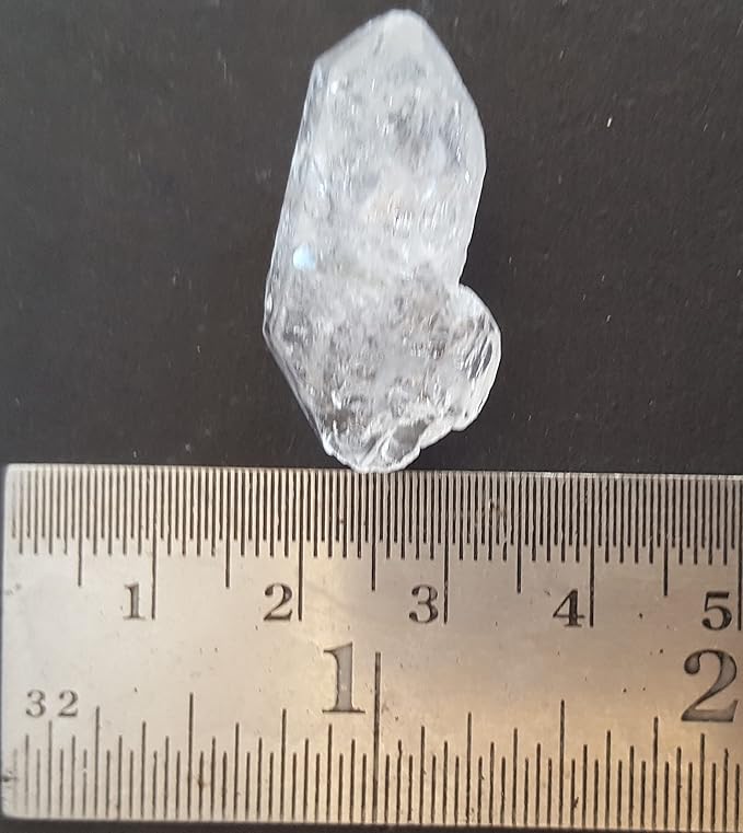 A Herkimer diamond gemstone, undrilled and rough, positioned on a table with a ruler.
