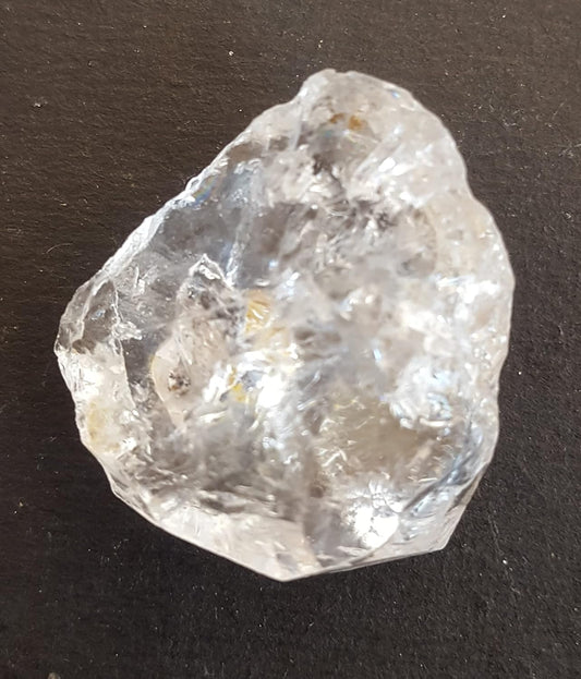 A Herkimer diamond stone bead on a table, featuring its unpolished surface and striking clarity, capturing light beautifully.