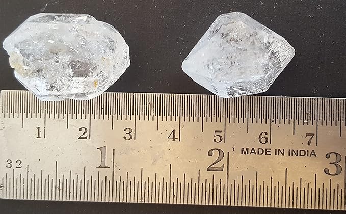 Two large white Herkimer Diamond crystals are being measured with a ruler, showcasing their size and clarity