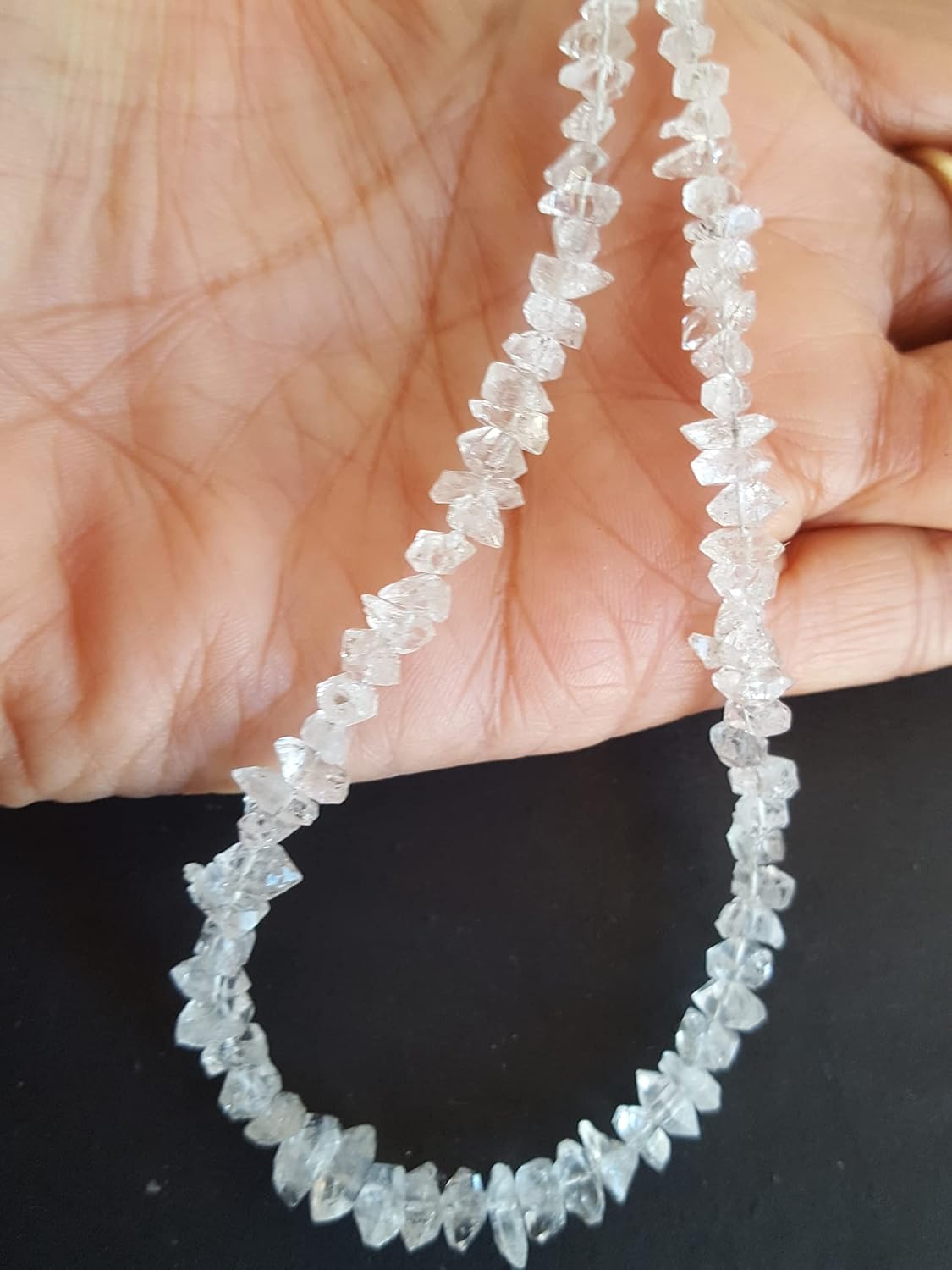 A hand displays a rough Herkimer Diamonds strand, with beads measuring 6-8mm in diameter.
