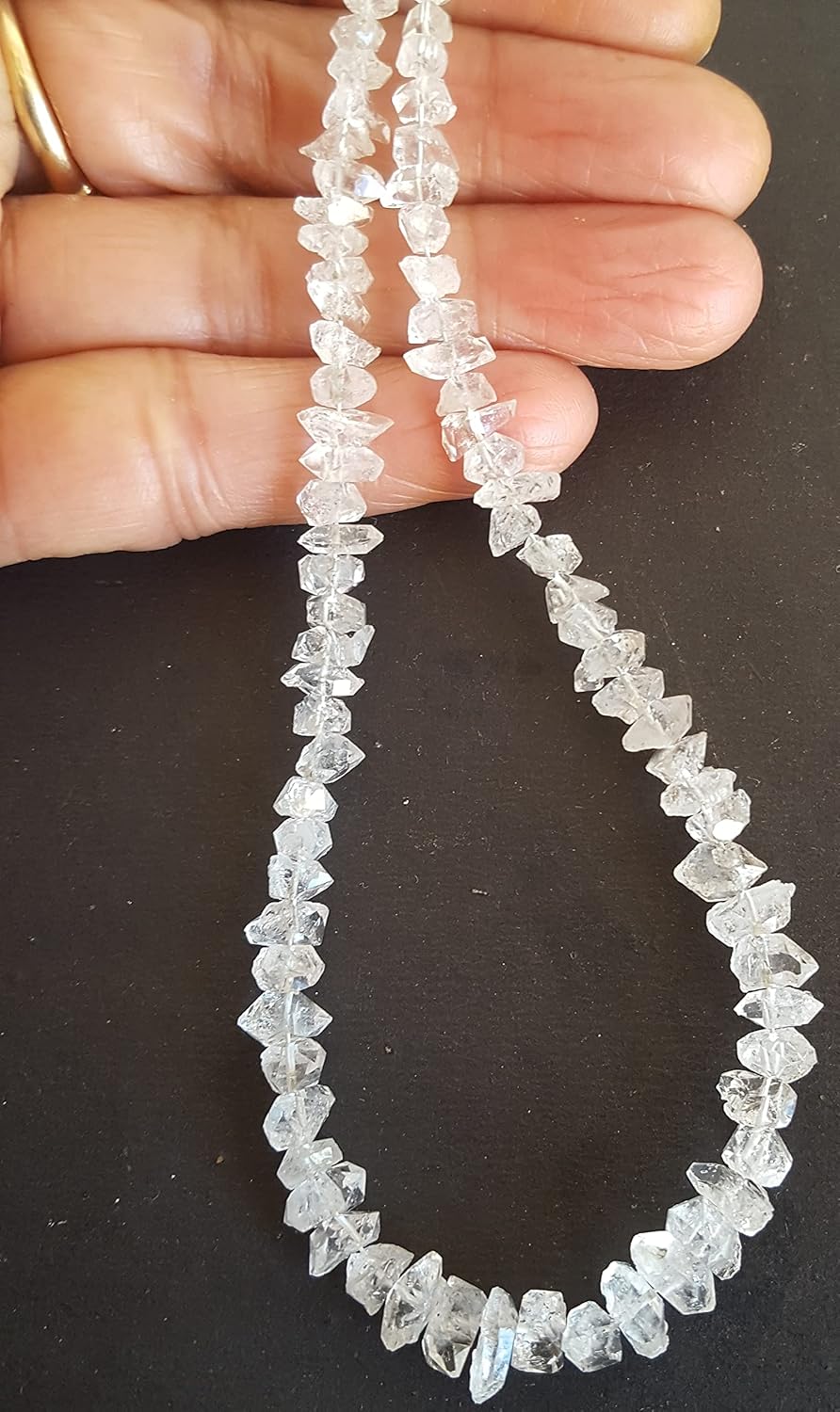 Close-up of a hand grasping a strand featuring rough Herkimer Diamonds, each 6-8mm in size.