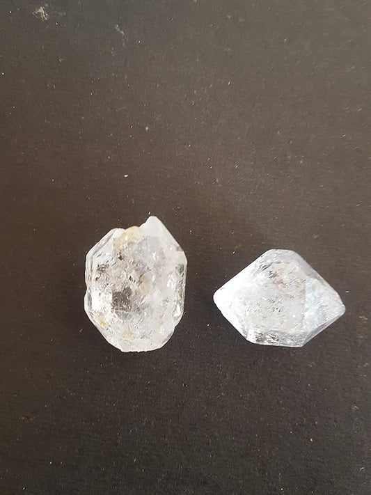 Two loose gemstone, clear Herkimer Diamond, resting on a smooth black surface.