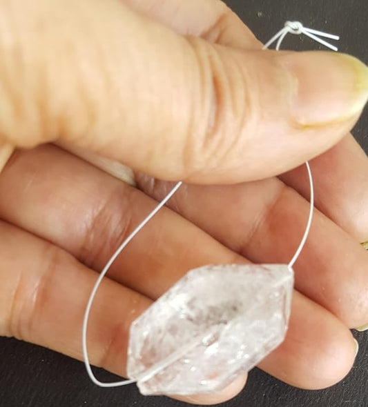 Herkimer Diamond rough gemstone bead with a centre-drilled hole, held in hand against a dark background.