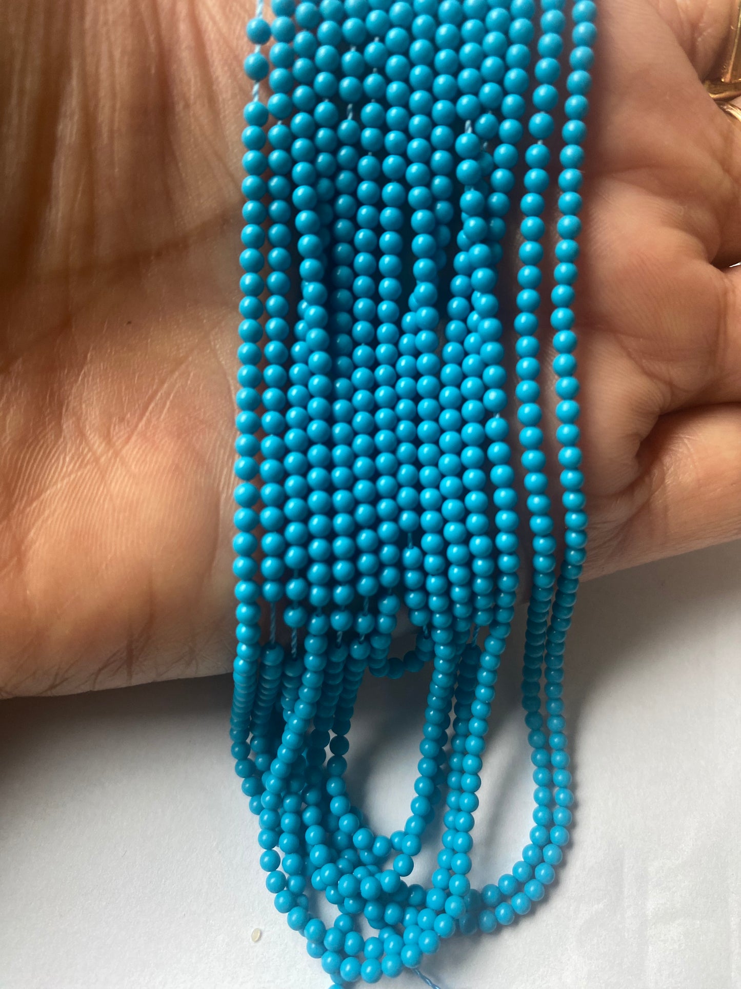 A person holding a vibrant bunch of 2.3mm Smooth Round Howlite Turquoise beads.