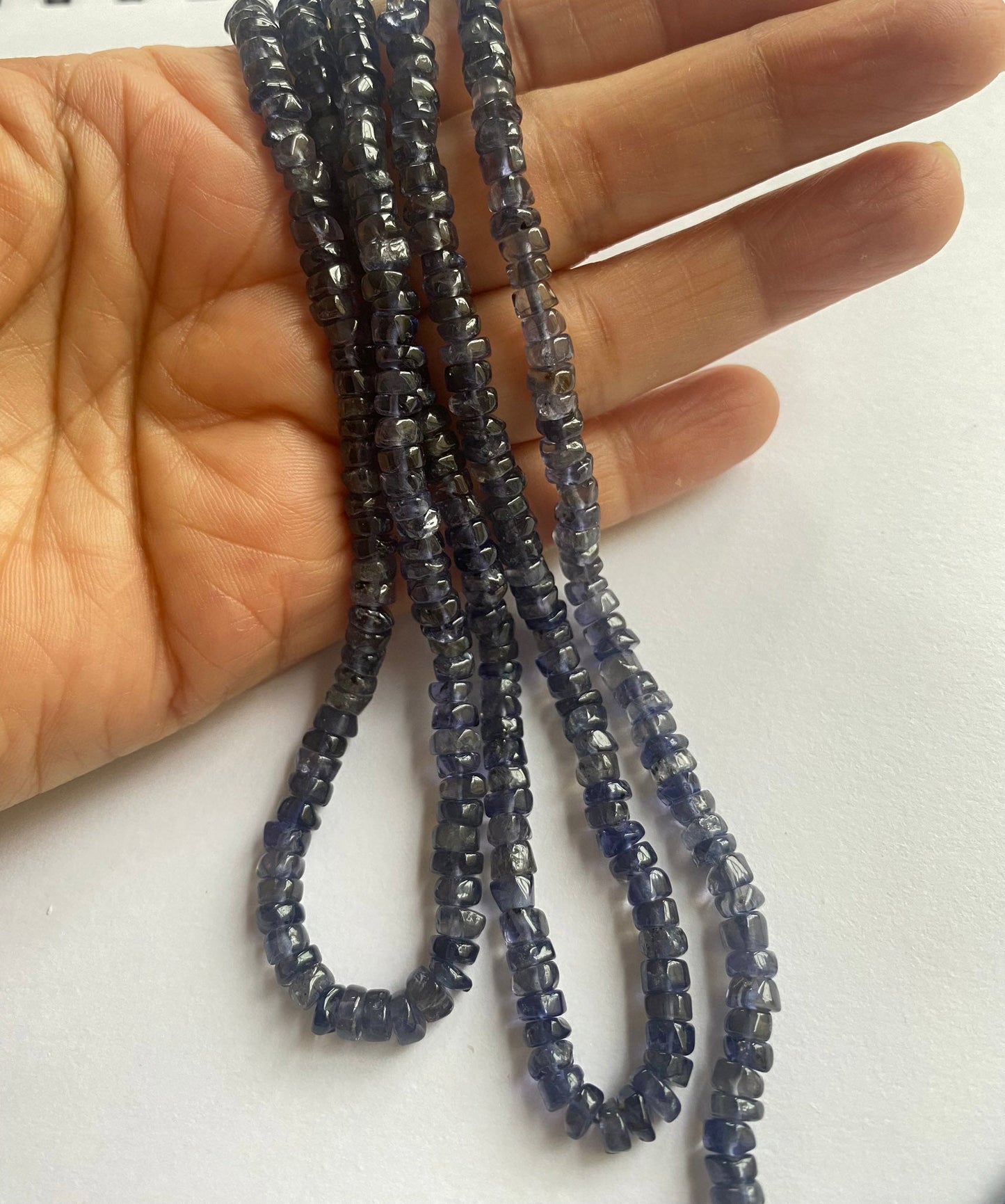 Premium iolite smooth wheel beads, 5 to 5mm, arranged in strands to display their deep blue tones and superior gemstone craftsmanship