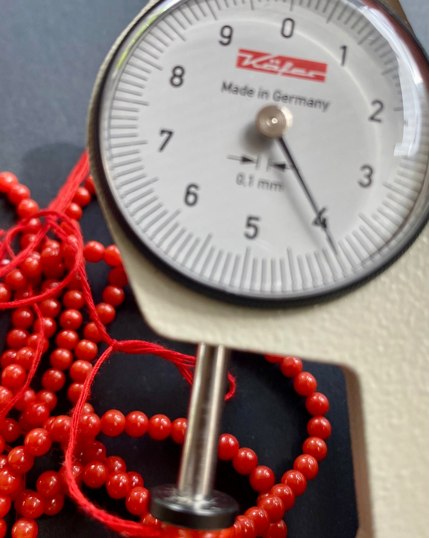 A close-up view of a measuring dial gauge with shiny red 4mm Italian coral beads scattered around it.
