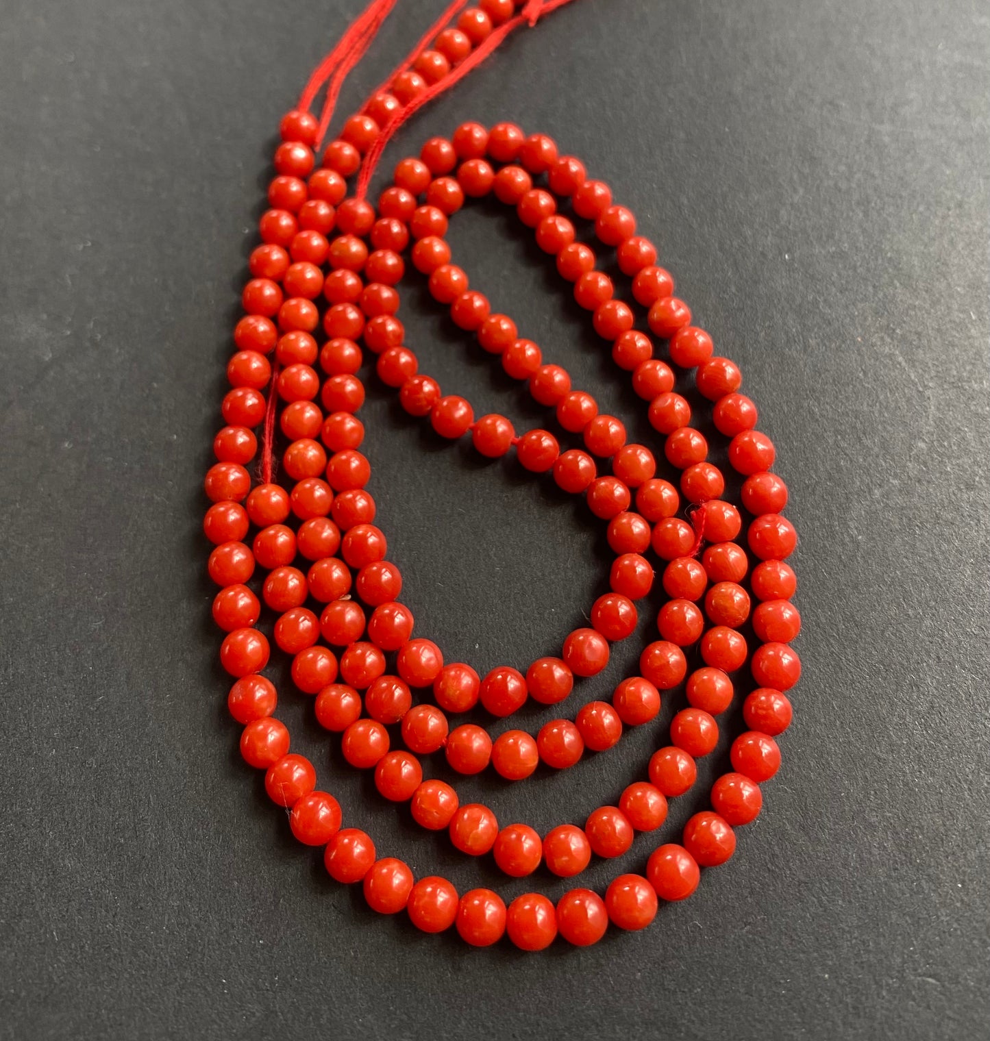 A close-up of a necklace featuring red beads displayed on a sleek black surface, highlighting its vibrant colour contrast.