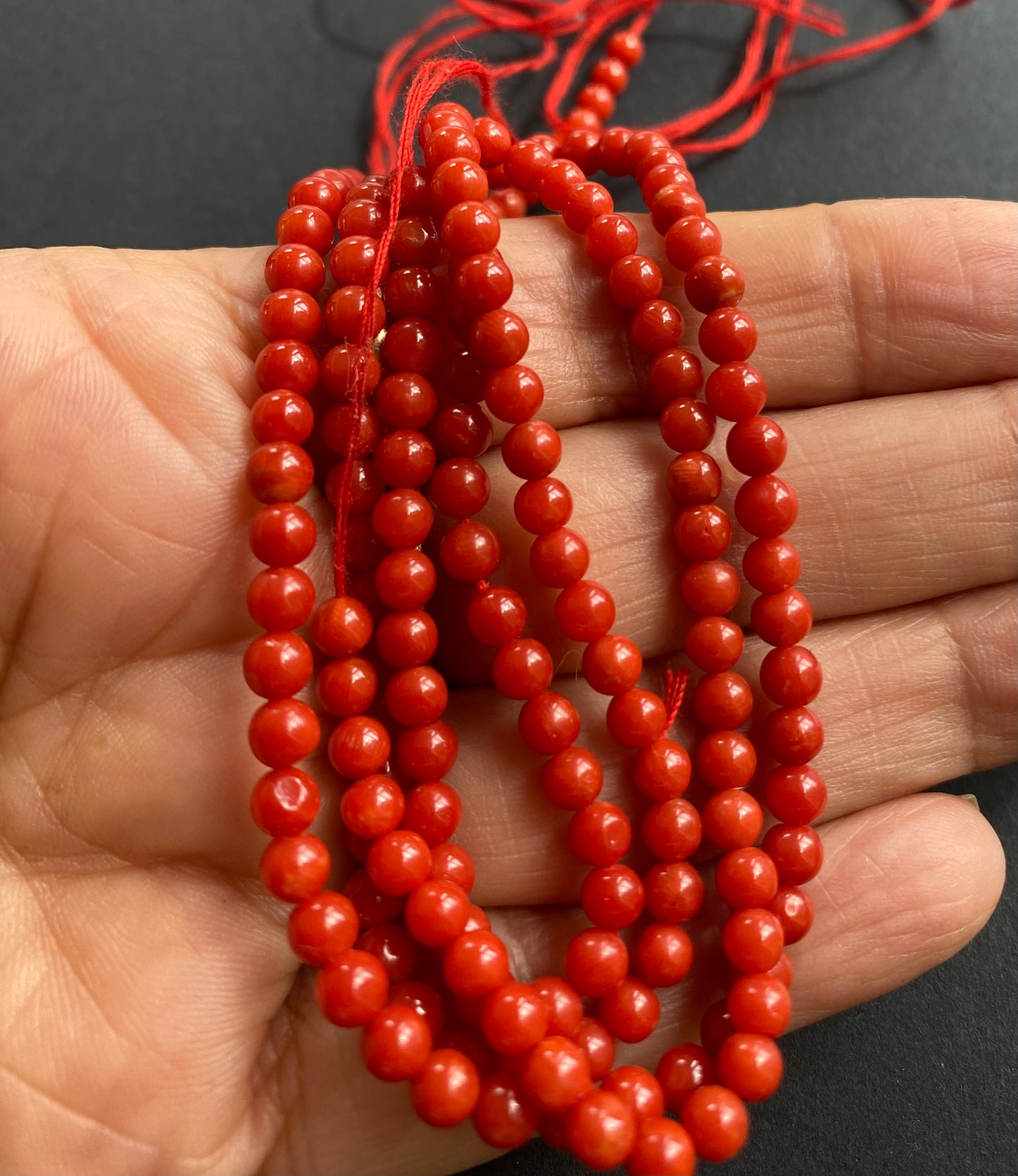 A hand holding a strand of smooth, round 4mm red coral beads, showcasing their vibrant colour and elegant design.