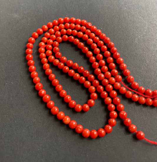 A striking necklace with red beads resting on a black surface, showcasing the vivid colours and elegant design.