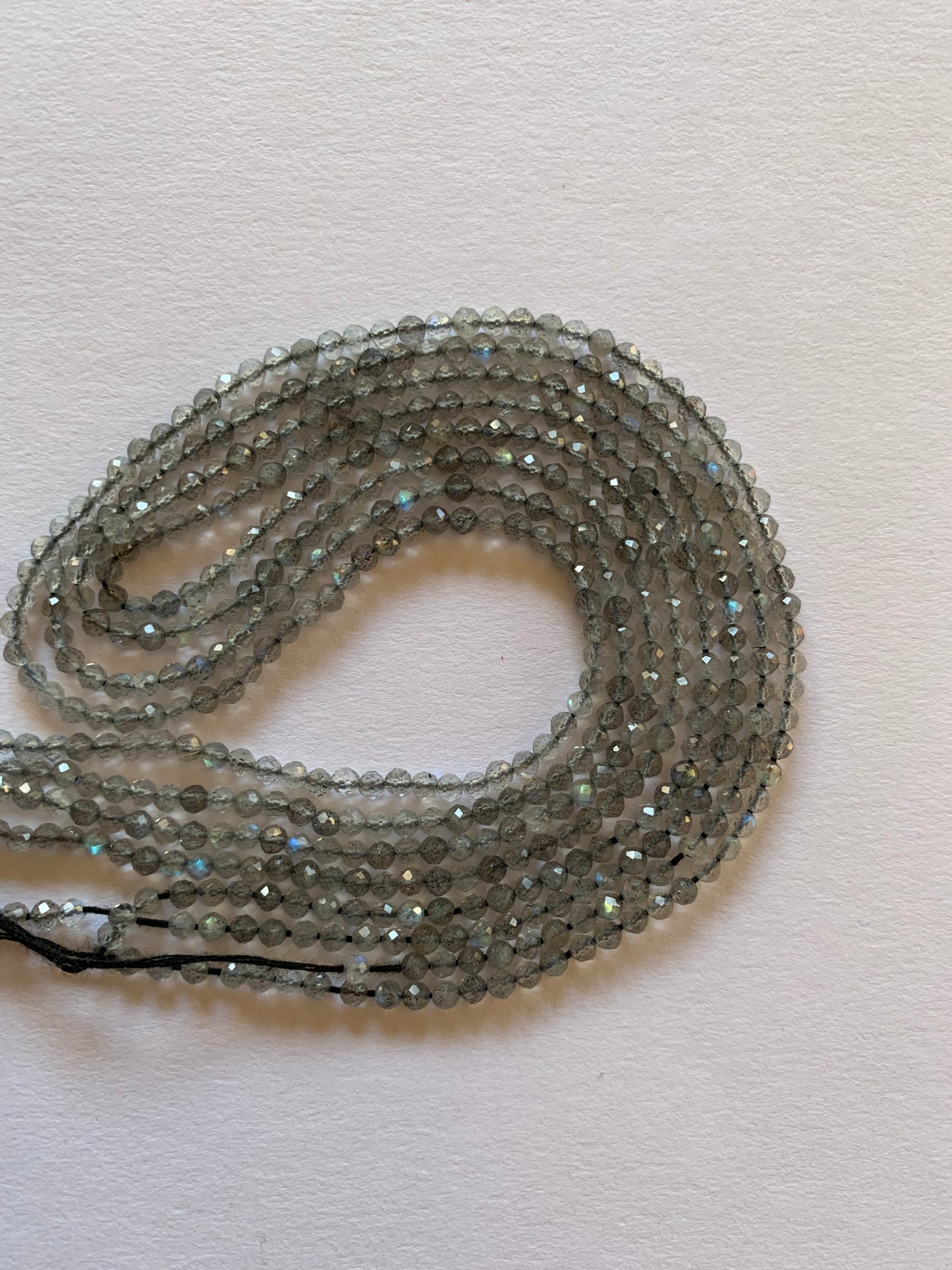 Beautiful strands of 2.5-2.7mm Labradorite beads on a white surface, emphasising their subtle lustre and elegance.