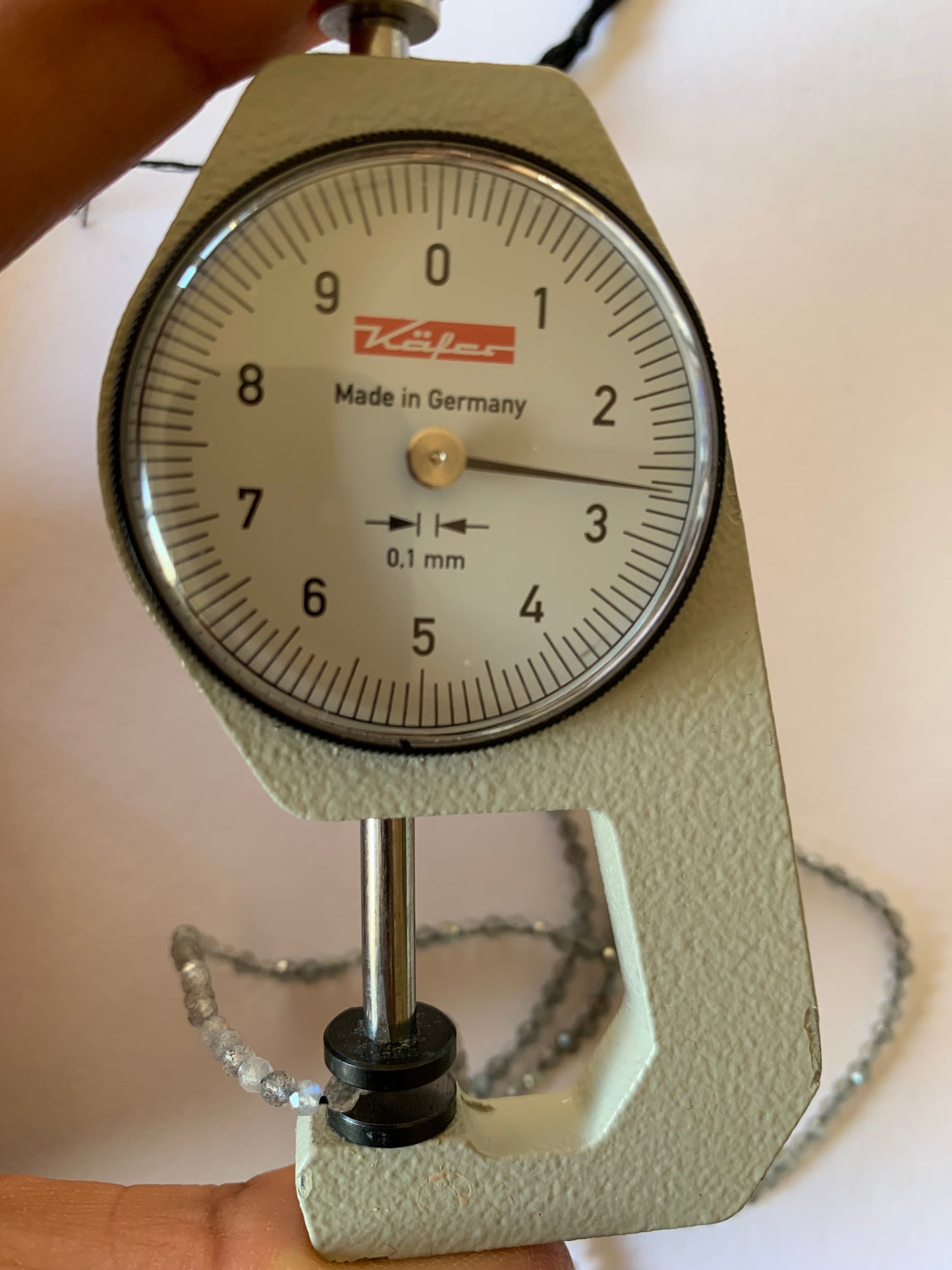 A person uses a dial gauge to measure a Labradorite Faceted Rondelle, sized between 2.5-2.7mm.
