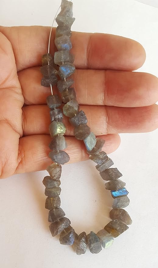 A hand holding a strand of rough centre-drilled labradorite beads, showcasing their unique iridescent colours.