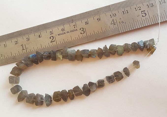 A ruler alongside rough, centre-drilled labradorite gemstone beads, emphasising their vibrant hues and distinctive patterns of the semi-precious stones.