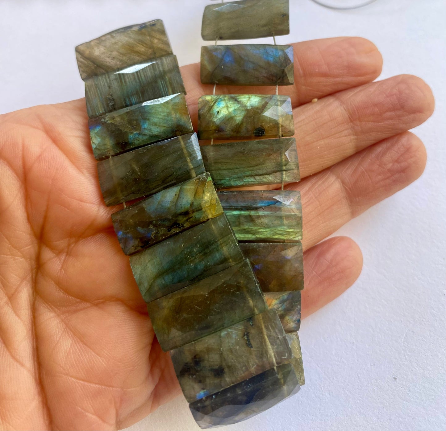 Labradorite rectangle-cut beads with crisp facets and grey base tones, laid out in rows.