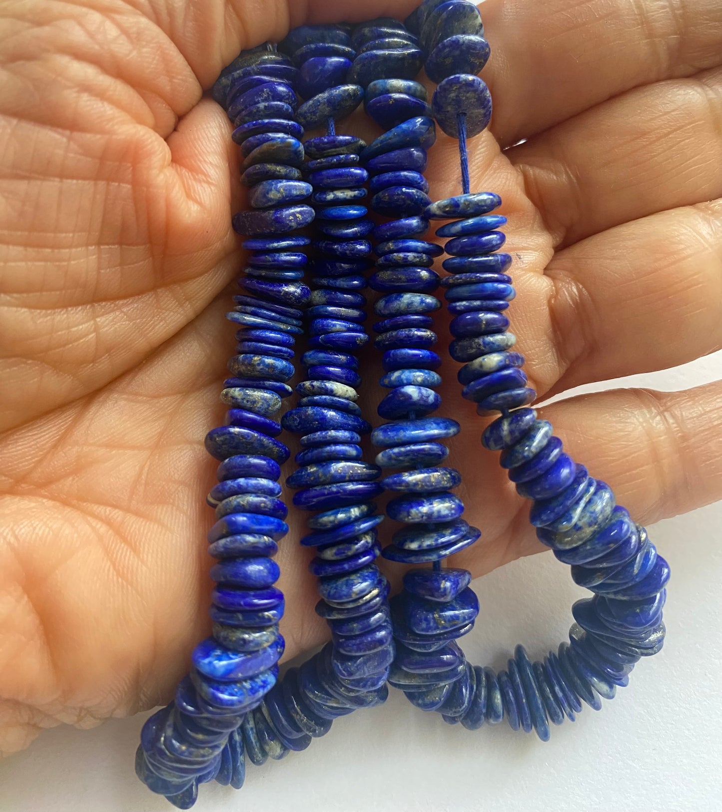 A person holding a smooth strand of Lapis Heishi Smooth beads, measuring 8-10mm, showcasing their elegant blue colour.