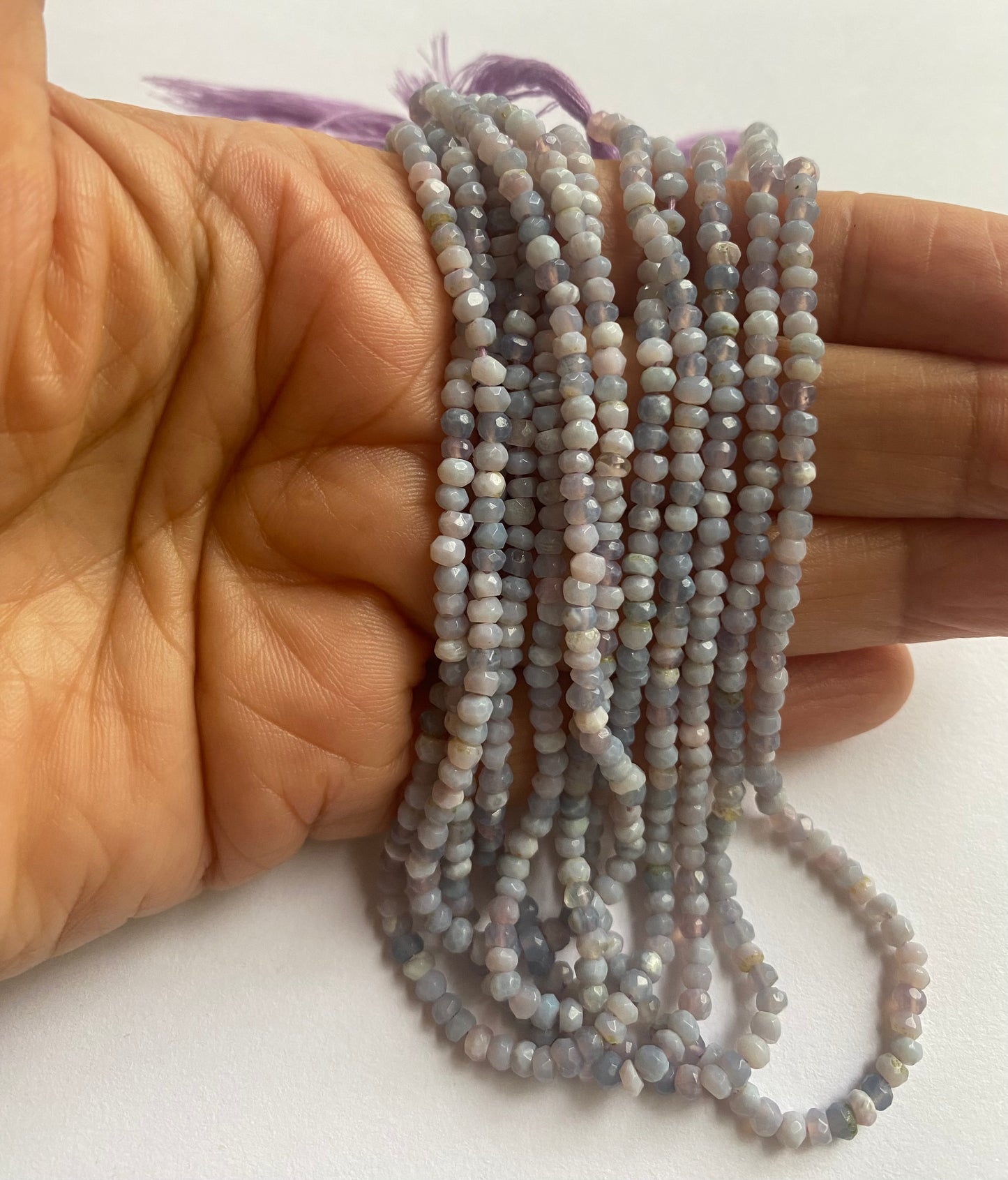 A hand holding Lavender Opal 3.0-3.2mm beads with Faceted Rondelle for intricate jewellery and gemstone craft projects.