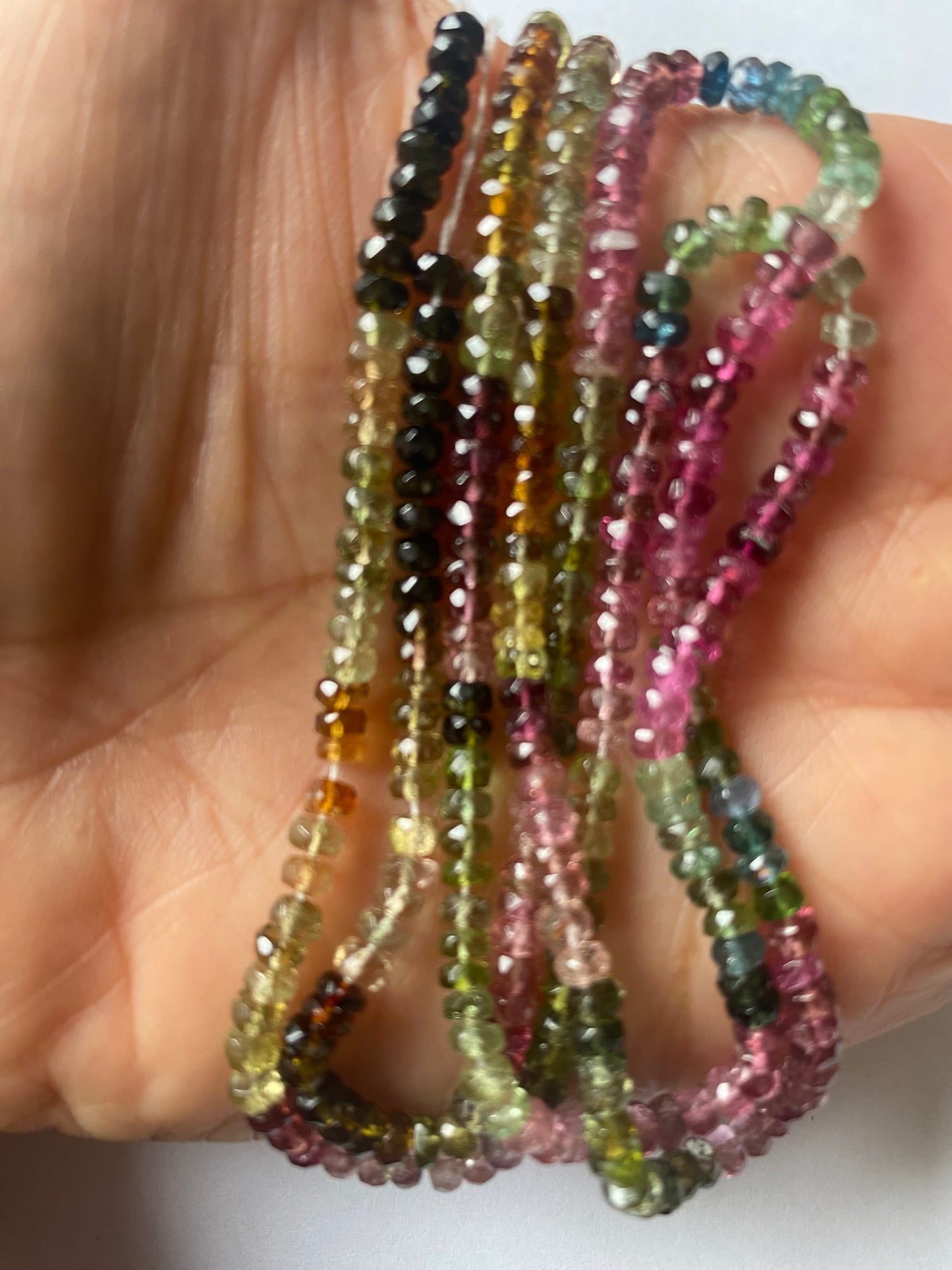 Close-up of a person’s hand showcasing a colourful assortment of 3.5mm micro-cut tourmaline beads.