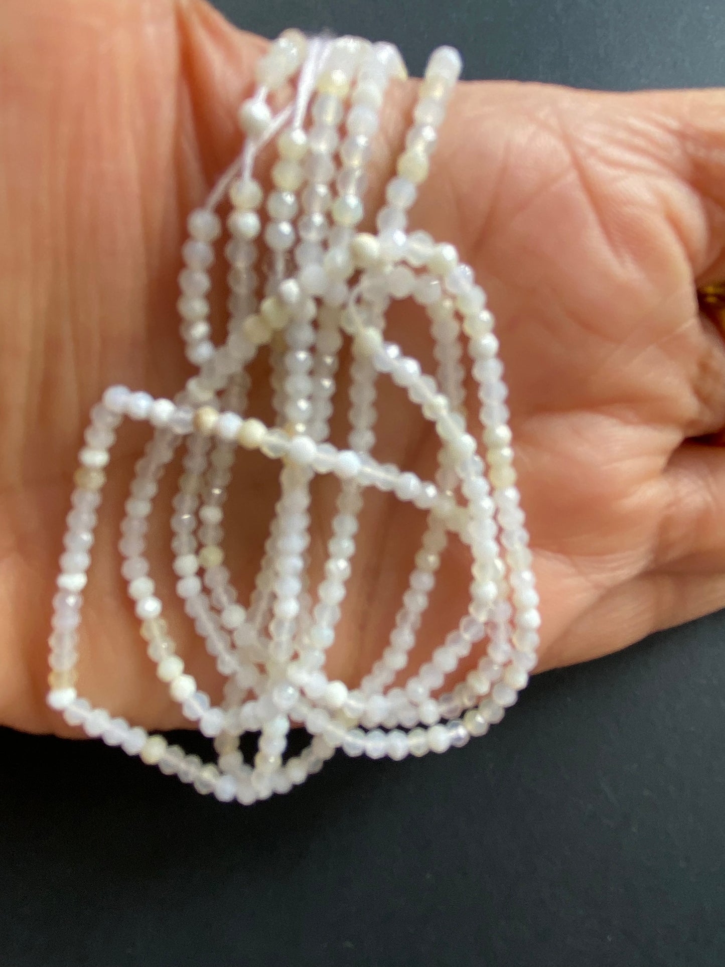 A person holding a strand of micro-faceted opal rondelle beads, measuring 2.6-2.7mm in size.