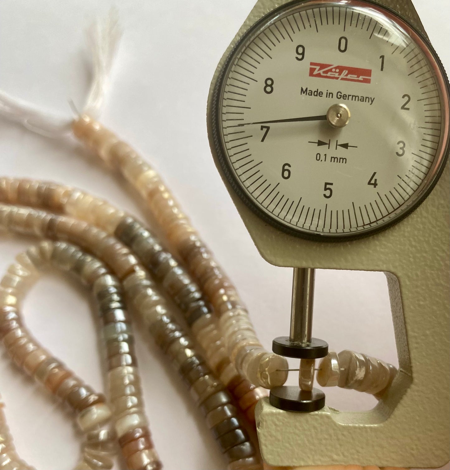 A person measures a moonstone smooth wheel stone, 7mm, using a dial gauge measuring tool.